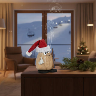 Räuchermännchen „Knallkopp Klausi“ (9 cm), farbig gestaltet mit roter Weihnachtsmütze und witzigem Gesichtsausdruck, rauchend auf einem Tisch vor winterlicher Wohnkulisse dekoriert.