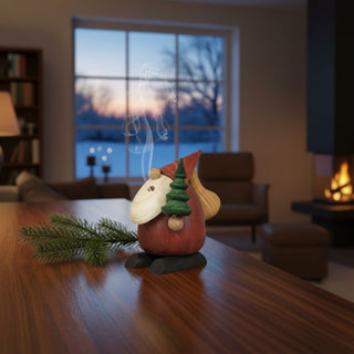 Räuchermännchen „Baumlieferservice“ (10 cm), farbig gestaltet mit kleinem Tannenbaum und Sack, rauchend auf einem Tisch in gemütlicher Wohnumgebung dekoriert.
