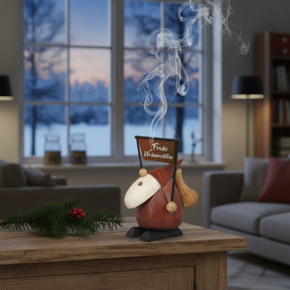Räuchermännchen „Frohe Weihnachten“ (10 cm), farbig gestaltet mit Schild „Frohe Weihnachten“ und Sack auf dem Rücken, rauchend auf einem Tisch in gemütlicher Wohnatmosphäre dekoriert.