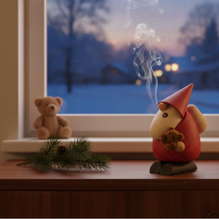 Räuchermännchen „Weihnachtsmann – Teddybär“ (11 cm), farbig gestaltet mit roter Mütze und kleinem Teddybär in der Hand, rauchend auf einer Fensterbank vor winterlicher Abendkulisse dekoriert.