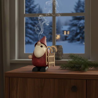 Räuchermännchen „Weihnachtsmann mit Schlitten“ (11 cm), farbig gestaltet mit roter Mütze und kleinem Holzschlitten, rauchend auf einem Tisch vor winterlicher Fensterkulisse dekoriert.