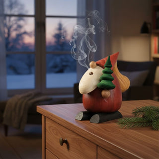 Räuchermännchen „Weihnachtsmann – Baumlieferservice“ (24 cm), farbig gestaltet mit kleiner Tanne und Sack, rauchend auf einem Tisch vor gemütlicher Wohnkulisse dekoriert.