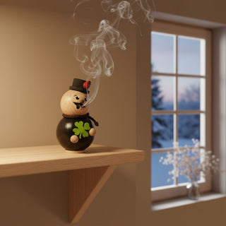 Räuchermännchen Mini „Schornsteinfeger“ (8 cm), farbig gestaltet mit Zylinder und Glücksklee, rauchend auf einem Tisch vor winterlicher Fensterkulisse dekoriert.
