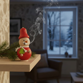 Räuchermännchen Mini „Weihnachtsmann“ (8 cm), farbig gestaltet mit roter Mütze und Tannenmotiv, rauchend auf einem Regal vor winterlicher Fensterkulisse dekoriert.