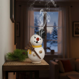 Räuchermännchen Mini „Schneemann“ (8 cm), farbig gestaltet mit Hut und Besen, rauchend auf einem Tisch vor winterlicher Fensterkulisse dekoriert.