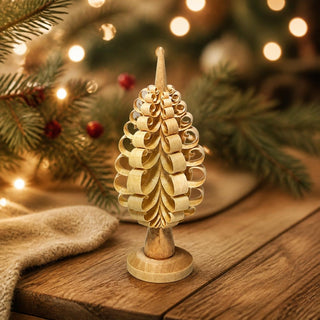Spanbaum aus hellem Holz auf rundem Standfuß, filigran aus Holzspänen gefertigt, dekoriert auf einem Holztisch vor warmen Weihnachtslichtern und Tannenzweigen.