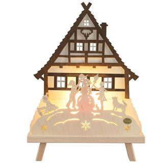 Standleuchte Waldhaus aus Holz. Indirekt durch LED beleuchtet zeigt zentral Kinder, die Schneemannbauen, das Hauptmotiv ist eine Wandhaus im Hintergrund.