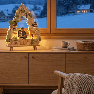 LED-Standleuchte „DEFA-Schneewittchen“ aus farbig gestaltetem Holz (41 cm) mit warmweißer LED-Beleuchtung. Das detailreiche Motiv zeigt Szenen aus dem Märchen Schneewittchen, darunter Schneewittchen und den Prinzen sowie weitere Figuren und Elemente einer märchenhaften Wald- und Berglandschaft. Die Leuchte ist in Form eines geschwungenen Bogens gestaltet und mit farbigen Akzenten versehen. Sie steht auf einem Sideboard vor einem Fenster mit Blick auf eine verschneite Winterlandschaft.