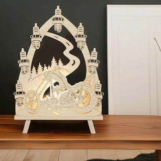 LED-Standleuchte „(N)Ostalgie Chopper-Freund“ aus naturfarbenem Holz (41 cm) mit warmweißer LED-Beleuchtung. Das filigran ausgeschnittene Motiv zeigt einen klassischen Chopper auf einer Straße vor einer Kulisse aus Nadelbäumen und einer geschwungenen Landstraße. Mehrere stilisierte Zündkerzen bilden einen dekorativen Rahmen um die Szene. Die Leuchte steht auf einem Holztisch vor einer dunklen Wand und setzt das nostalgische Motorradmotiv mit ihrem warmen Licht stimmungsvoll in Szene.