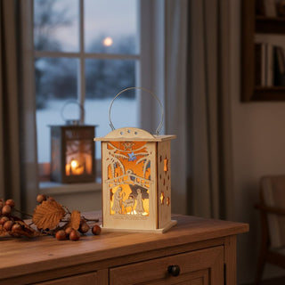 Laterne für 1 Teelicht oder mit LED‑Stripe „Christi Geburt“, 16 cm, aus naturbelassenem Holz mit filigraner Krippenszene mit Maria, Josef und dem Kind unter einem Stern, dekorativ auf einem Holzsideboard mit Zweigen und Nüssen platziert, vor einem Fenster mit winterlicher Landschaft und warm leuchtendem Licht im Inneren.