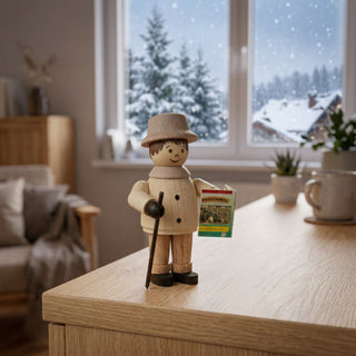 Miniatur „Wanderer“ (ca. 5 cm) aus naturbelassenem Holz, mit kleiner Figur in Winterkleidung, Hut, Wanderstock und einer Karte in der Hand. Die Figur steht auf einem Holzmöbel in einer gemütlichen Stube; im Hintergrund ein Fenster mit verschneiter Winterlandschaft sowie Möbel und Dekoration, die eine ruhige, winterliche Atmosphäre schaffen.