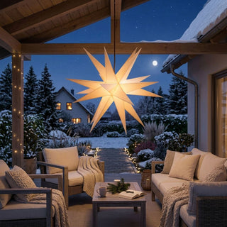 Weißer LED-Adventsstern für den Außenbereich von SAICO mit 60 cm Durchmesser, aufgehängt unter einer überdachten Terrasse. Der festlich beleuchtete Stern strahlt warmweißes Licht aus und bildet den Blickfang einer gemütlichen Winterlandschaft mit verschneitem Garten. Komfortable Loungemöbel, Decken und dezente Lichter entlang des Gartenwegs schaffen eine stimmungsvolle weihnachtliche Atmosphäre.