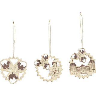 Der Baumbehang ist aus Holz, naturfarben und mit dezenten Akzenten versehen. Es gibt drei verschiedene Motive. Ein Aufhänger zeigt die drei Haselnüsse. Der Zweite zeigt den Prinzen und die drei Haselnüsse und das dritte Bild zeigt das Schloss Moritzburg mit den drei Haselnüssen.