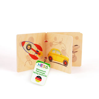 „Ein kleines Holz-Bilderbuch für Kinder mit Fahrzeugillustrationen. Auf der linken Seite ist eine bunte Rakete mit einem lächelnden Gesicht im Fenster zu sehen, auf der rechten Seite ein gelbes Auto. Auf der nächsten Seite ist teilweise ein Flugzeug abgebildet. Ein Etikett am Buch trägt die Aufschrift: ‚HESS Bilderbuch Fahrzeuge, farbig bedruckt 100 % MADE IN GERMANY‘.“