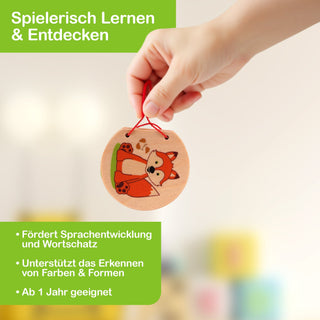 „Eine Hand hält eine runde Holzscheibe mit der Illustration eines Fuchses. Im Hintergrund sind unscharfe, bunte Objekte zu sehen. Im Bild steht der Text: ‚Spielerisch Lernen & Entdecken – Fördert Sprachentwicklung und Wortschatz – Unterstützt das Erkennen von Farben & Formen – Ab 1 Jahr geeignet‘.“