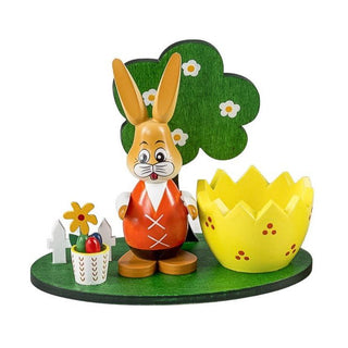 Gelber Eierbecher aus Holz mit kleinem Osterhäschen, Bäumchen und Ostereierkörbchen auf einem grünen Sockel
