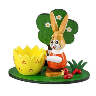 Gelber Eierbecher aus Holz mit kleinem Osterhäschen und Bäumchen auf einem grünen Sockel