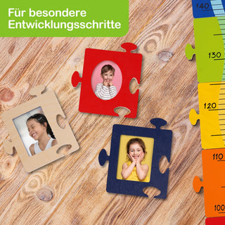 Drei Puzzleteile mit Kinderfotos liegen auf einem Holzboden. Die Puzzleteile sind beige, rot und blau. Oben links steht in weißer Schrift auf grünem Hintergrund: „Für besondere Entwicklungsschritte“. Rechts im Bild befindet sich eine farbige Messlatte.