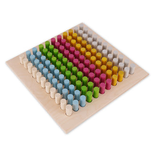 „Ein quadratisches Holzbrett mit einem Raster aus 10 Reihen und 10 Spalten. Darin stecken bunte, zylindrische Stifte in den Farben Weiß, Blau, Grün, Pink und Gelb. Die Farben sind jeweils diagonal über das Brett angeordnet.“