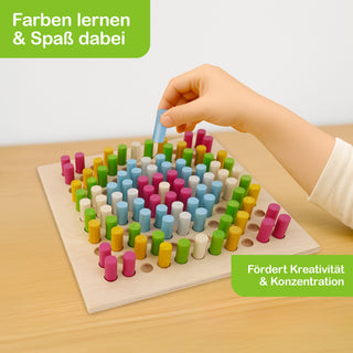 „Ein Kind hält einen blauen Holzstift und steckt ihn in ein Loch auf einem Holzbrett, das mit vielen bunten Stiften bestückt ist. Oben links im Bild steht in einem grünen Feld: ‚Farben lernen & Spaß dabei‘. Unten rechts steht: ‚Fördert Kreativität & Konzentration‘.“