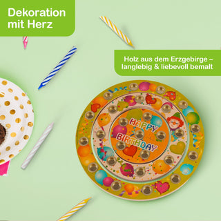 Runde, bunte Geburtstagsdekoration aus Holz mit Kerzenhaltern und der Aufschrift „HAPPY BIRTHDAY“ in der Mitte. Um die Dekoration liegen farbige Geburtstagskerzen und ein Teller mit goldenen Punkten. Oben links steht „Dekoration mit Herz“, oben rechts „Holz aus dem Erzgebirge – langlebig & liebevoll bemalt“.