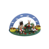 Grüne Blumenwiese mit blauen Himmelsbogen, 2 gelbfarbenen Teelichthaltern und einer farbigen Hasenschule, bestehend aus 3 süßen Osterhasen und kleinen frühlingshaften Details