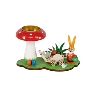 Grünfarbener Sockel mit einem Fliegenpilz als Teelichthalter und einem Osterhasen mit Wagen