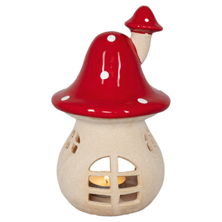 Ein 20 cm hoher Kerzenhalter aus Terracotta in Form eines Pilzes. Der Pilzhut ist rot mit weißen Punkten, die Basis ist beige und hat Fensteröffnungen. Im Inneren befindet sich ein Teelicht, dessen Licht durch die Fenster scheint.