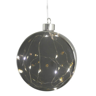 Runder, grauer LED-Glastaler mit feiner, warmweiß leuchtender Lichterkette im Inneren. Der Glastaler hängt an einem dünnen Faden und erzeugt durch das getönte Glas eine dezente Lichtstimmung. 