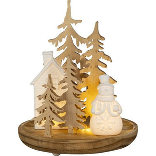 LED-Holz-Arrangement mit beleuchtetem Keramikhaus und Schneemann auf 24 cm Holzsockel, umgeben von Holzbaum-Silhouetten – winterliche Szene mit stimmungsvoller Beleuchtung.