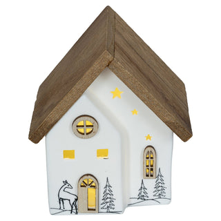 Weißes LED-Keramikhaus mit schwarzer Linienzeichnung eines Hirsches und Bäumen, Holzdach, sternförmigen Lichtausschnitten und gelbem Lichtschein aus den Fenstern, batteriebetrieben mit Timer, 10,7 cm hoch.