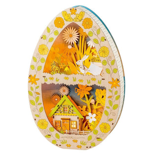 Batteriebetriebenes Holz-Osterei mit 3D Optik. Zu sehen ist ein Haus mit Blumen und eine Osterase mit einer Ostereierarre in frühlingshaften Grün- und Gelbtönen