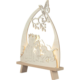 Die LED Standleuchte "Katzenfreund" aus Holz, zeigt drei süße Kätzchen, die im Gras sitzen – eines davon spielt mit einem kleinen Mäuschen, während ein Schmetterling auf einem Baumast mit Blättern sitzt. Beleuchtete Schrägansicht.