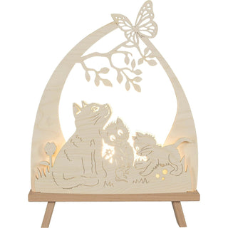 Die LED Standleuchte "Katzenfreund" aus Holz, zeigt drei süße Kätzchen, die im Gras sitzen – eines davon spielt mit einem kleinen Mäuschen, während ein Schmetterling auf einem Baumast mit Blättern sitzt. Beleuchtete Frontalansicht.