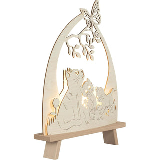 Die LED Standleuchte "Katzenfreund" aus Holz, zeigt drei süße Kätzchen, die im Gras sitzen – eines davon spielt mit einem kleinen Mäuschen, während ein Schmetterling auf einem Baumast mit Blättern sitzt. Beleuchtete Schrägansicht.