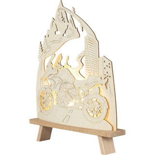 LED Standleuchte "Motorradfreund". Mit einer Höhe von 41 cm und gefertigt aus Holz, zeigt sie ein dynamisches Motorrad im Mittelpunkt der Szene. Im Hintergrund verläuft eine stilisierte Straße, die sich durch eine beeindruckende Berglandschaft schlängelt – ein Hinweis auf eine abenteuerliche Bergroute, die zum Träumen einläd. Beleuchtete Schrägansicht.