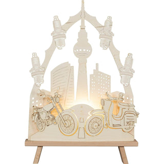 Die holzige Standleuchte (N)Ostalgie in Natur, stellt ein Simson-Moped und eine Schwalbe auf dem Weg nach Berlin dar. Mittig ist das Ziel dargestellt. Der Fernsehturm ragt deutlich heraus. Seitlich und als Umrandung der Spitze sind Zündkerzen passend zum Thema eingearbeitet. Unter Beleuchtung kann man sich diese spannende Reise durchaus real vorstellen.