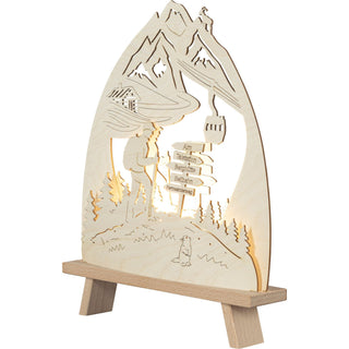 LED Standleuchte aus Holz zeigt Berglandschaft mit einem Wanderer auf einem Wanderweg, Wegweisern und einer stilisierten Seilbahn. Schrägansicht, rechtsseitig, beleuchtet.