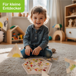 Ein kleines Kind sitzt auf einem Teppichboden in einem hellen Raum und spielt mit einem sechseckigen Puzzle mit bunten Bildern. Im Hintergrund sind Holzspielzeuge und ein Regal sichtbar. Oben links im Bild steht in weißer Schrift auf grünem Hintergrund: „Für kleine Entdecker“.