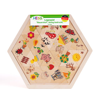Sechseckiges Holzpuzzle mit 24 Teilen und bunten Bauernhofmotiven. Zu sehen sind unter anderem eine Kuh, ein Schwein, ein Traktor, eine Blume, ein Haus sowie verschiedene Tiere wie Hühner und Schafe. Oben auf dem Puzzle befindet sich ein Etikett mit der Aufschrift „HESS Legespiel 'Bauernhof', farbig bedruckt, 24-tlg.“.
