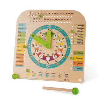 Hölzerne Lernuhr mit grünen Zeigern, bunten Zahlenkreisen für Minuten und Stunden, farbigen Monats- und Wochentagsleisten, vier Jahreszeitenfeldern und Symbolen für verschiedene Wetterlagen. Ein grüner Holzstab liegt davor.