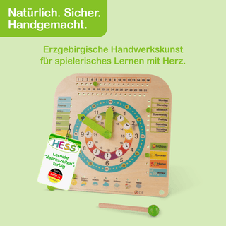 Farbig gestaltete Lernuhr aus Holz mit grünen Zeigern und Kreisen für Stunden und Minuten. Links sind die Monate, rechts die Wochentage und Jahreszeiten dargestellt. Oben steht: „Natürlich. Sicher. Handgemacht.“ und darunter: „Erzgebirgische Handwerkskunst für spielerisches Lernen mit Herz“. Ein Schild unten links zeigt: „HESS Lernuhr 'Jahreszeiten', farbig – 100% MADE IN GERMANY“.