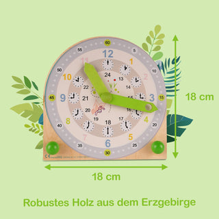 Runde Lernuhr aus Holz mit grünem Hintergrund und Blättermuster. Die Uhr hat grüne Zeiger und zwei grüne Knöpfe an der Basis. Die Zahlen 1–12 sind in Blau, 13–24 in Schwarz dargestellt. Kleine Zifferblätter zeigen jeweils vier Viertelstunden. Darunter steht der Text: „Robustes Holz aus dem Erzgebirge“.
