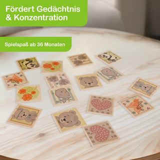 Ein Memory-Spiel mit 16 Karten liegt auf einem Holztisch. Die Karten zeigen bunte Illustrationen wie Bären, Pandas, Elefanten, Blumen und Herzen. Auf dem Bild steht: „Fördert Gedächtnis & Konzentration“ und „Spielspaß ab 36 Monaten“.