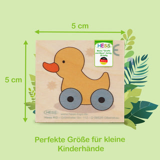  Ein quadratisches Holz-Memo-Spielstück (5 × 5 cm) zeigt eine gelbe Ente mit orangefarbenem Schnabel und blauen Rädern. Oben rechts steht „Hess Memo 'Giraffe und Maus', farbig, ab 2 Jahren“, unten „Perfekte Größe für kleine Kinderhände“.