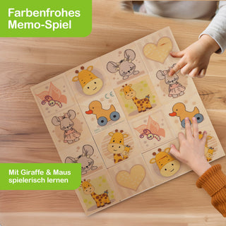 Ein farbenfrohes Memo-Spiel liegt auf einem Holztisch. Zwei Kinderhände spielen mit den Karten, die Motive wie Giraffe, Maus, Entenspielzeug und Herz zeigen. Oben links steht „Farbenfrohes Memo-Spiel“, unten links „Mit Giraffe & Maus spielerisch lernen“.