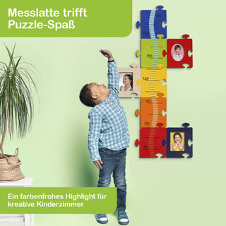 Ein Kind steht neben einer farbigen Messlatte aus Puzzleteilen an einer grünen Wand. Die Messlatte reicht von 70 cm bis 150 cm und ist in Blau, Gelb, Orange und Rot unterteilt. Auf jedem Puzzleteil ist ein Kinderfoto zu sehen. Links steht eine Pflanze in einem Korb auf einem weißen Tisch. Oben links steht „Messlatte trifft Puzzle-Spaß“, unten links „Ein farbenfrohes Highlight für kreative Kinderzimmer“.