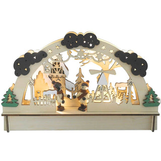 Beleuchteter LED-Holz-Lichterbogen mit filigranen Ausschnitten zeigt eine winterliche Dorfszene: Zwei kleine Figuren in Winterkleidung stehen im Zentrum, umgeben von Bäumen, einer Pyramide und Gebäuden. Der obere Bogen ist mit Wolken und Sternen verziert. Links und rechts am Sockel befinden sich grüne Bäume. 