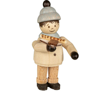 Eine Holzminiatur eines Jungen, der einen hellen Mantel, schwarze Schuhe und einen grauen Hut mit schwarzem Bommel trägt. Die Figur hat gemalte Gesichtszüge und hält eine Bratwurst in der Hand.