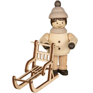 "Eine Holzfigur zeigt eine Person, die eine Wintermütze und einen Mantel trägt und einen kleinen Holzschlitten hält. Die Figur hat ein einfaches, handgefertigtes Aussehen mit bemalten Gesichtszügen und Kleidung. Der Schlitten ist ebenfalls aus Holz und hat ein detailliertes Design mit Latten für den Sitz und Kufen."